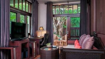 A room with a television, a desk, a chair, a sofa, and a large window with a view of trees.