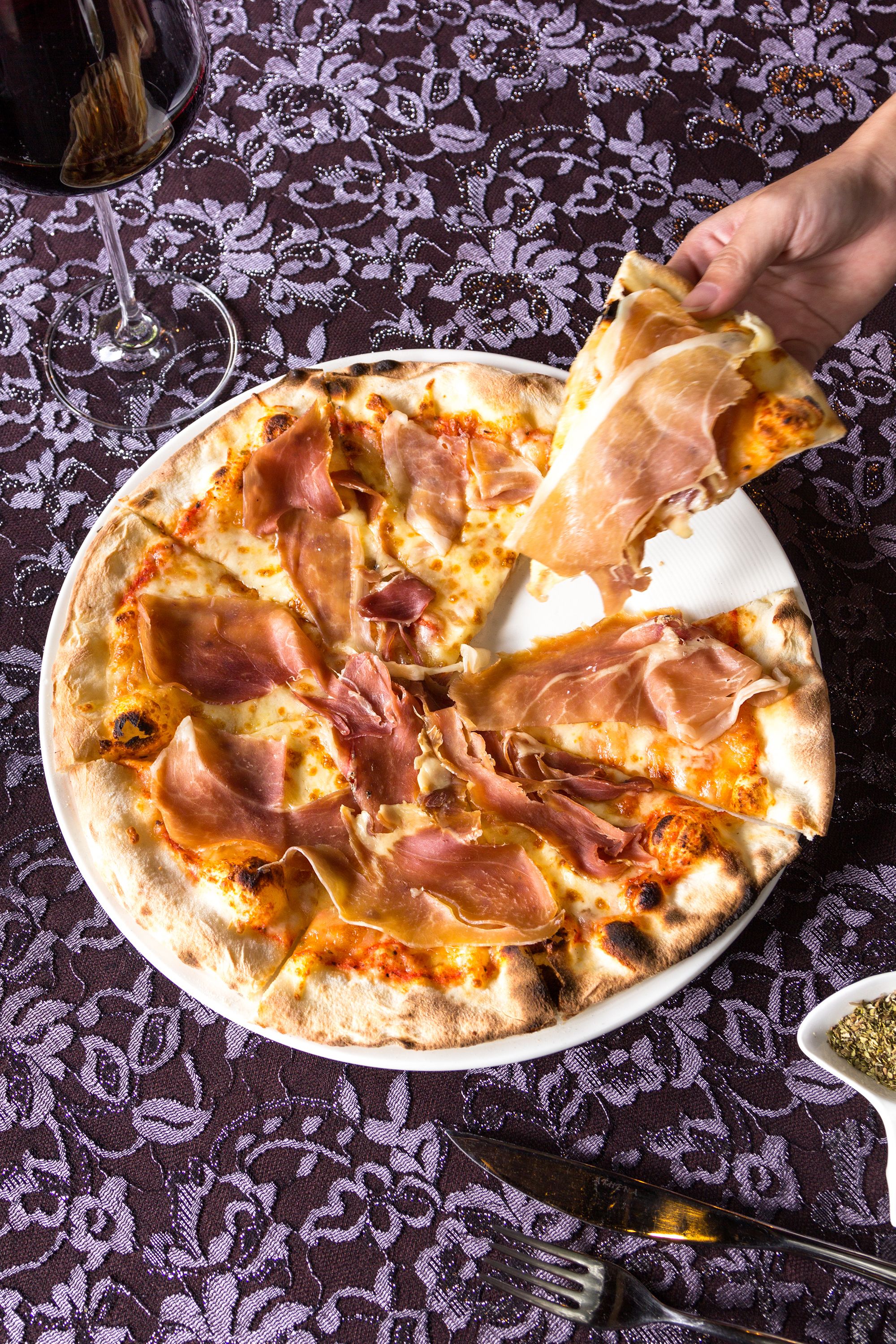 A pizza with ham slices on a patterned tablecloth.