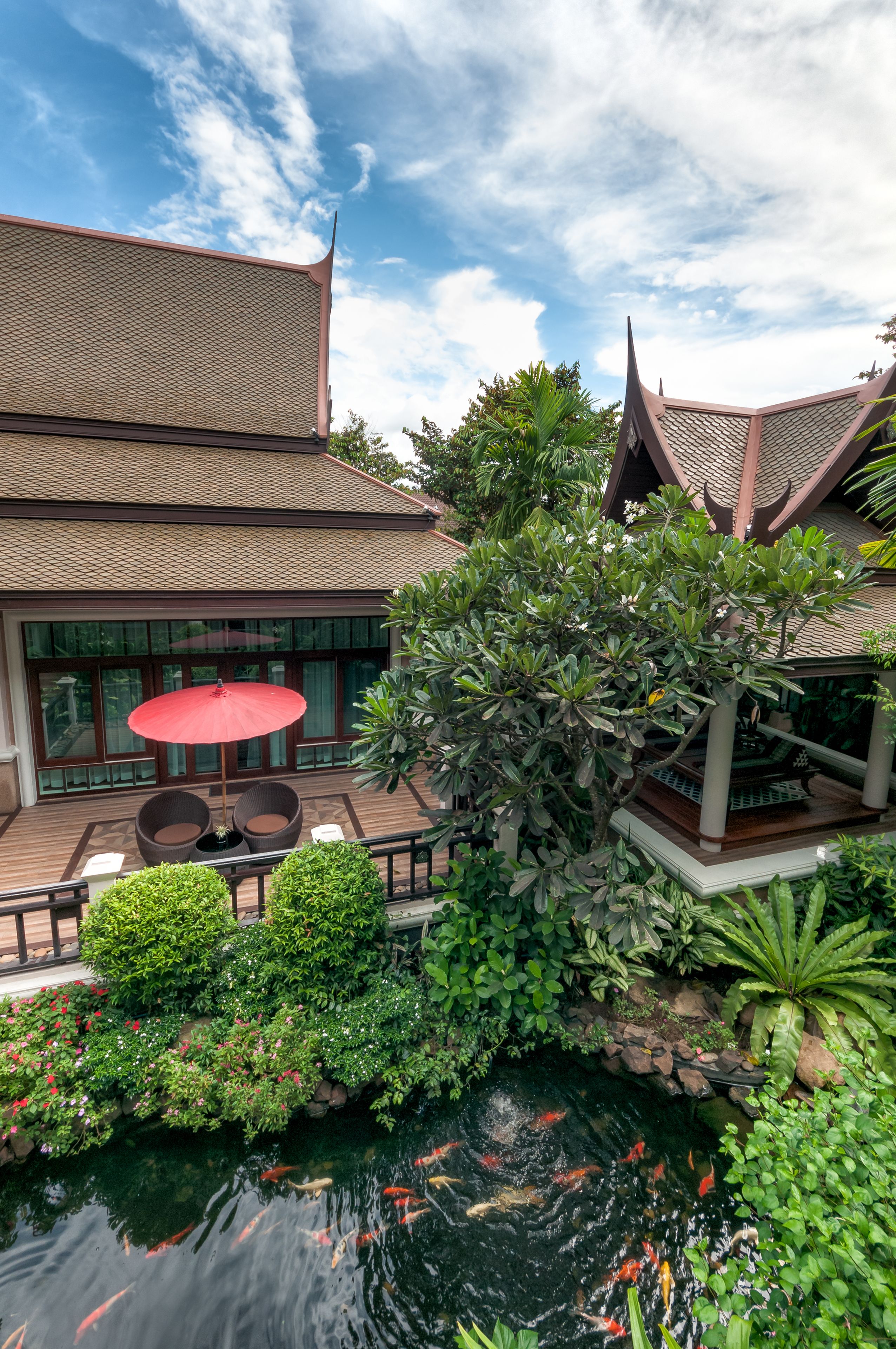 A traditional building with a tiled roof, a koi pond, and a red umbrella table.