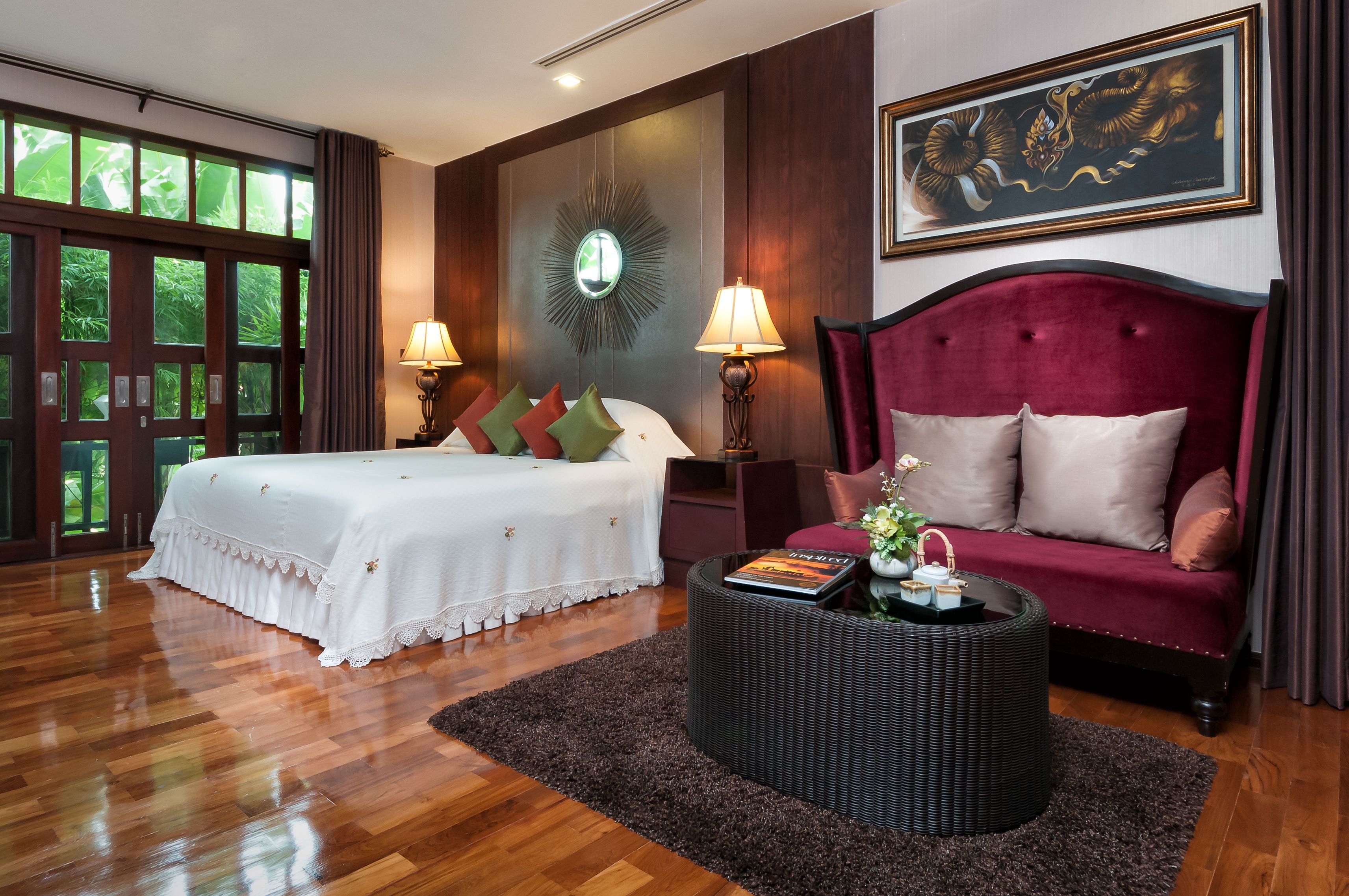 A hotel room with a bed, a sofa, a round coffee table, and a large window with a view of greenery.