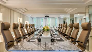 Un salón de conferencias con una larga mesa, sillas de cuero marrón y un centro de mesa floral.