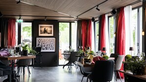 Un comedor moderno con techo de madera, ventanas amplias con cortinas rojas y una variedad de sillas y mesas.