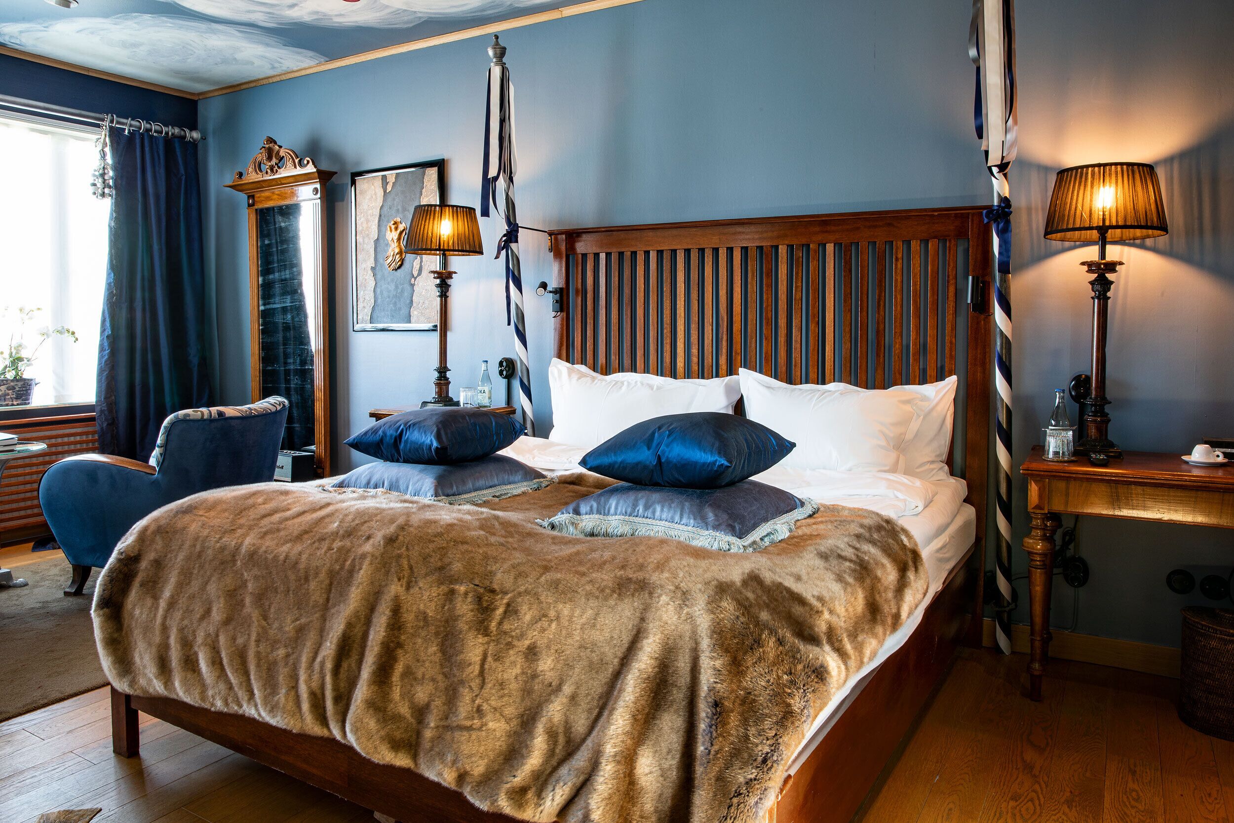 A bedroom with a large bed, two bedside lamps, a wooden headboard, and a blue chair.