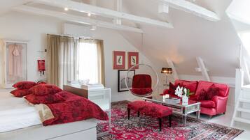 Un dormitorio con una cama grande, un sofá rojo, un sillón redondo y una alfombra estampada.