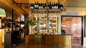 Una zona de bar con mostrador dorado, botellas de vino y copas.