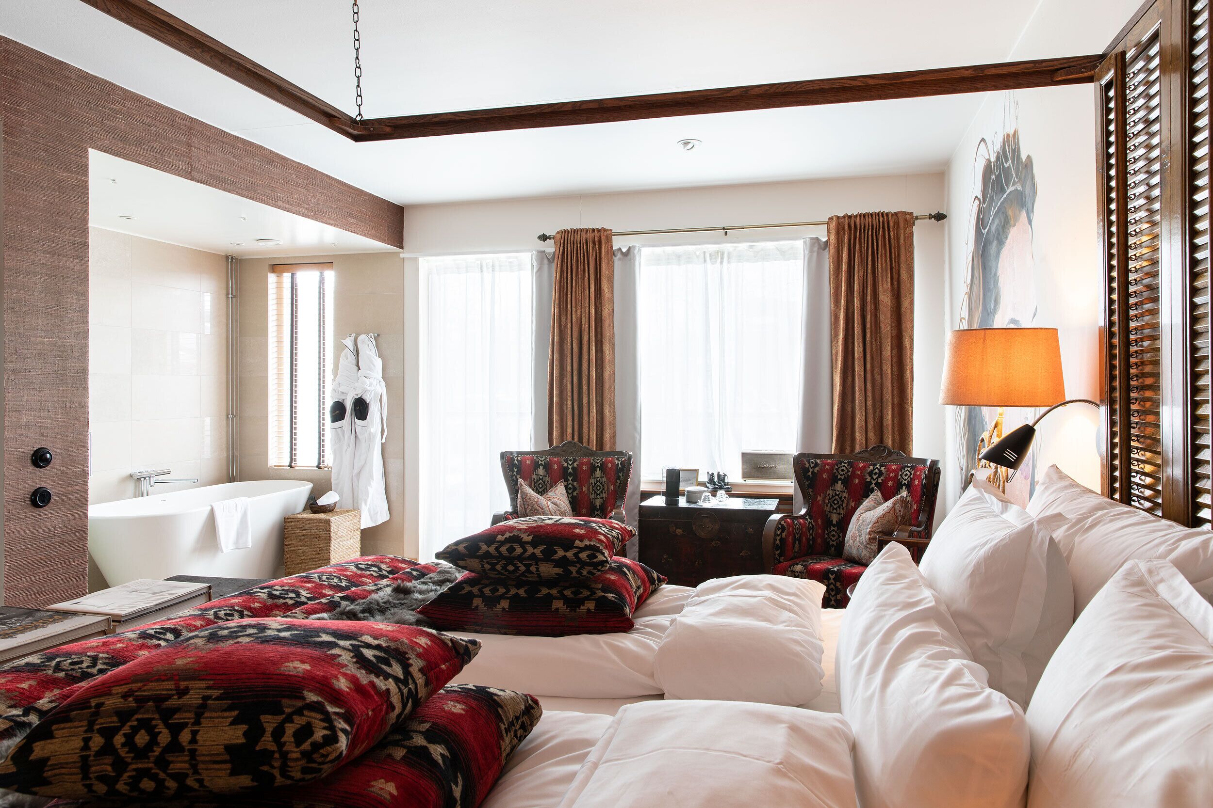 A hotel room with a large bed, a sitting area with a chair, a desk, and a bathtub.