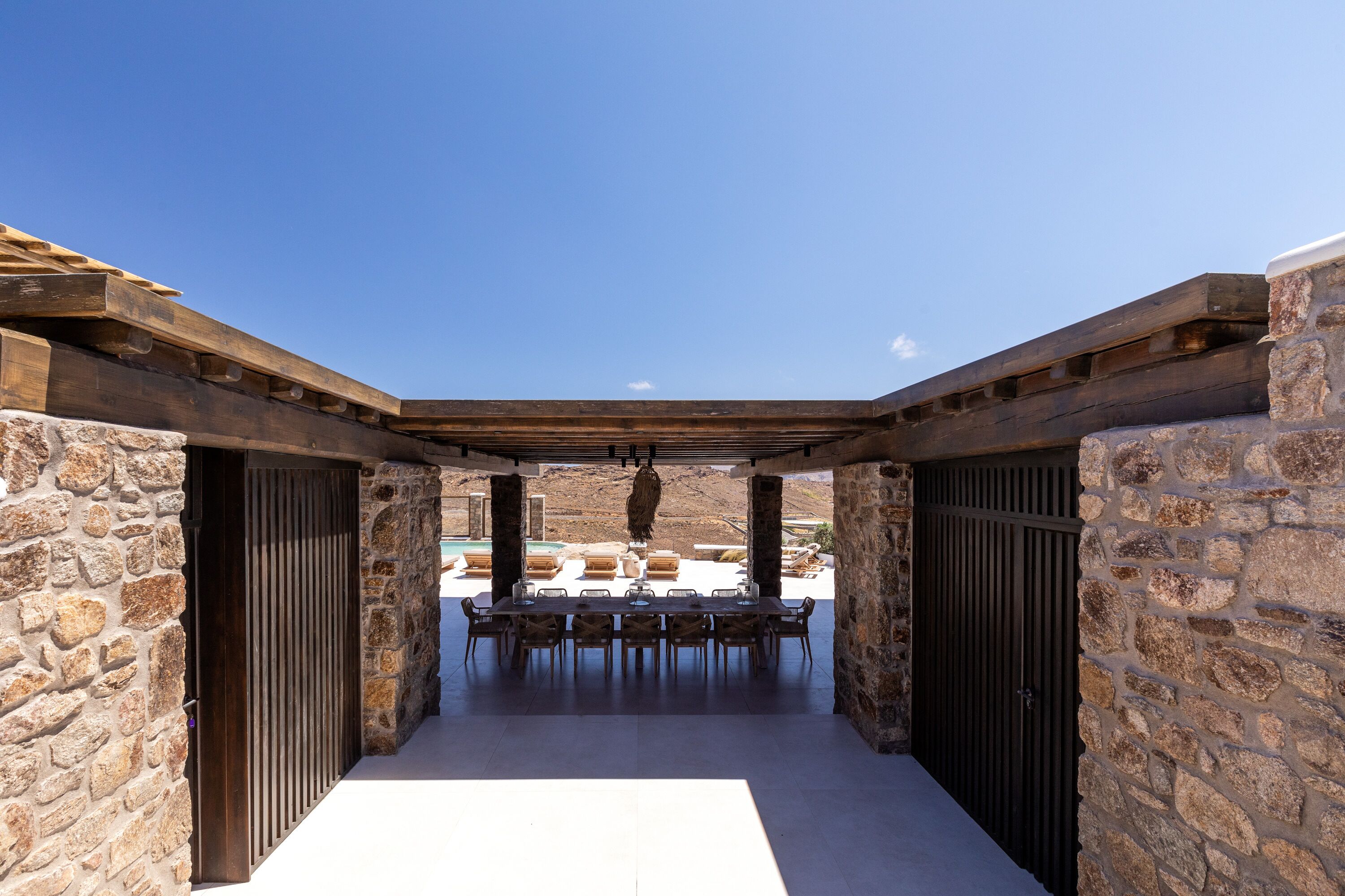 A covered outdoor dining area with stone walls and a long table.