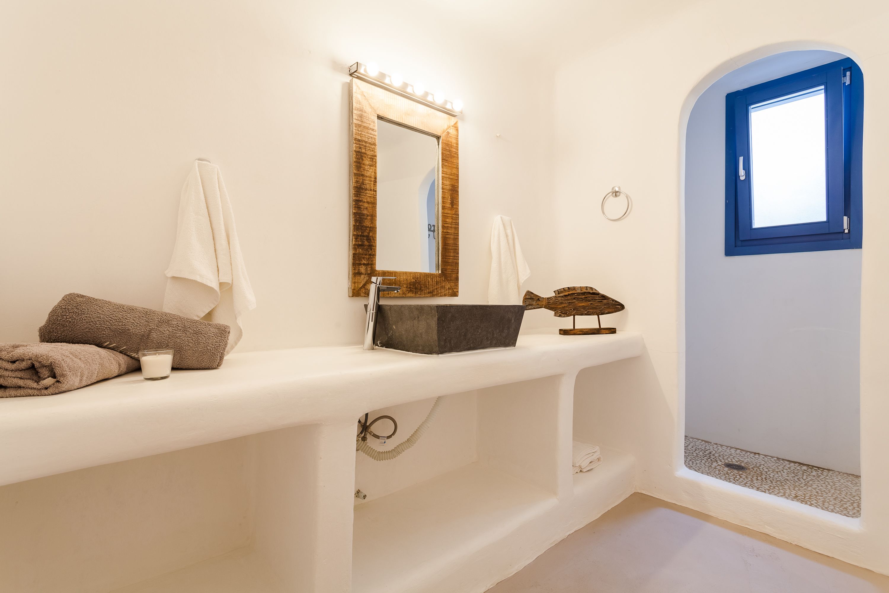 Un baño con tocador blanco, un espejo con iluminación, una toalla y una ventana pequeña.