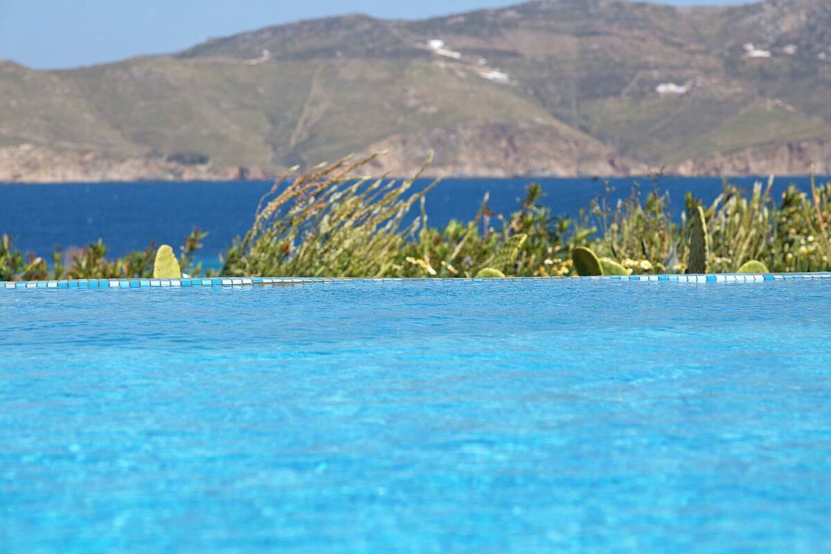 A swimming pool with clear blue water, surrounded by tropical plants and a mountainous landscape in the background.