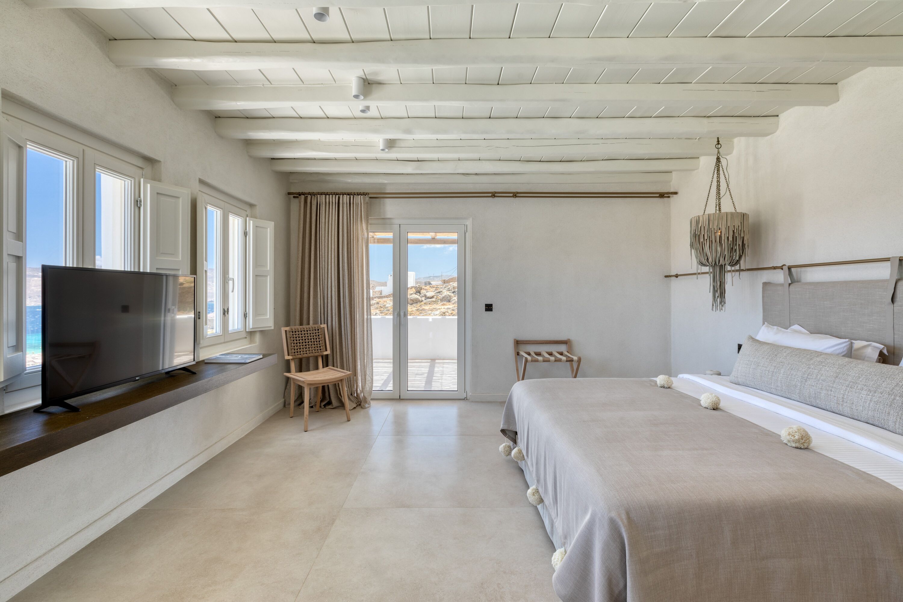 Un dormitorio con una cama grande, un televisor sobre una consola de madera, una silla y vistas al exterior por una puerta corrediza.
