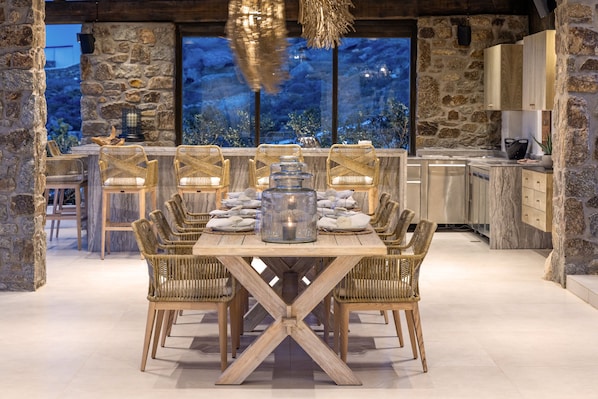 A dining area with a wooden table and wicker chairs, stone walls, and a view of the outdoors.