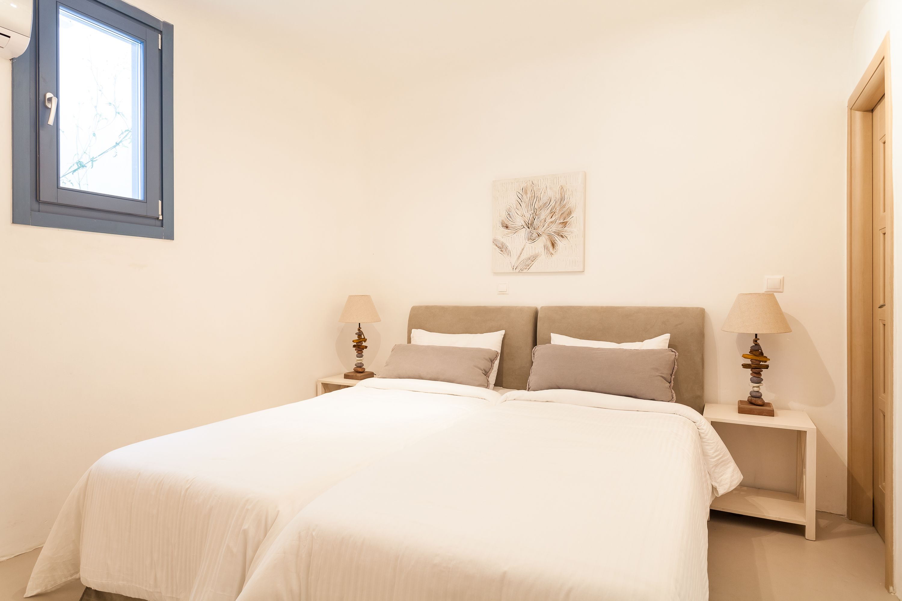A bedroom with a bed, two bedside tables, a window, and a wall-mounted artwork.