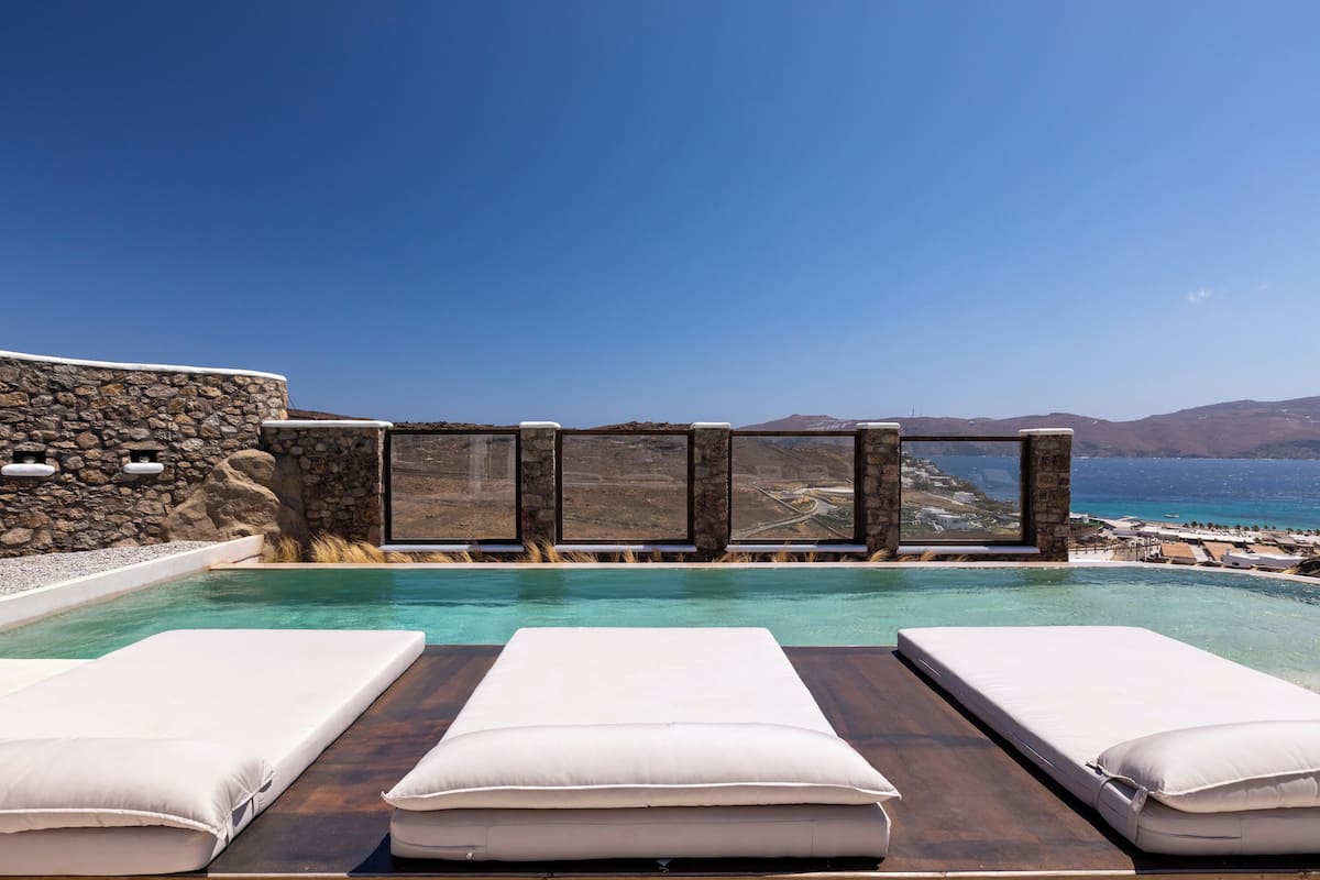 A pool with two lounge chairs and a stone wall.