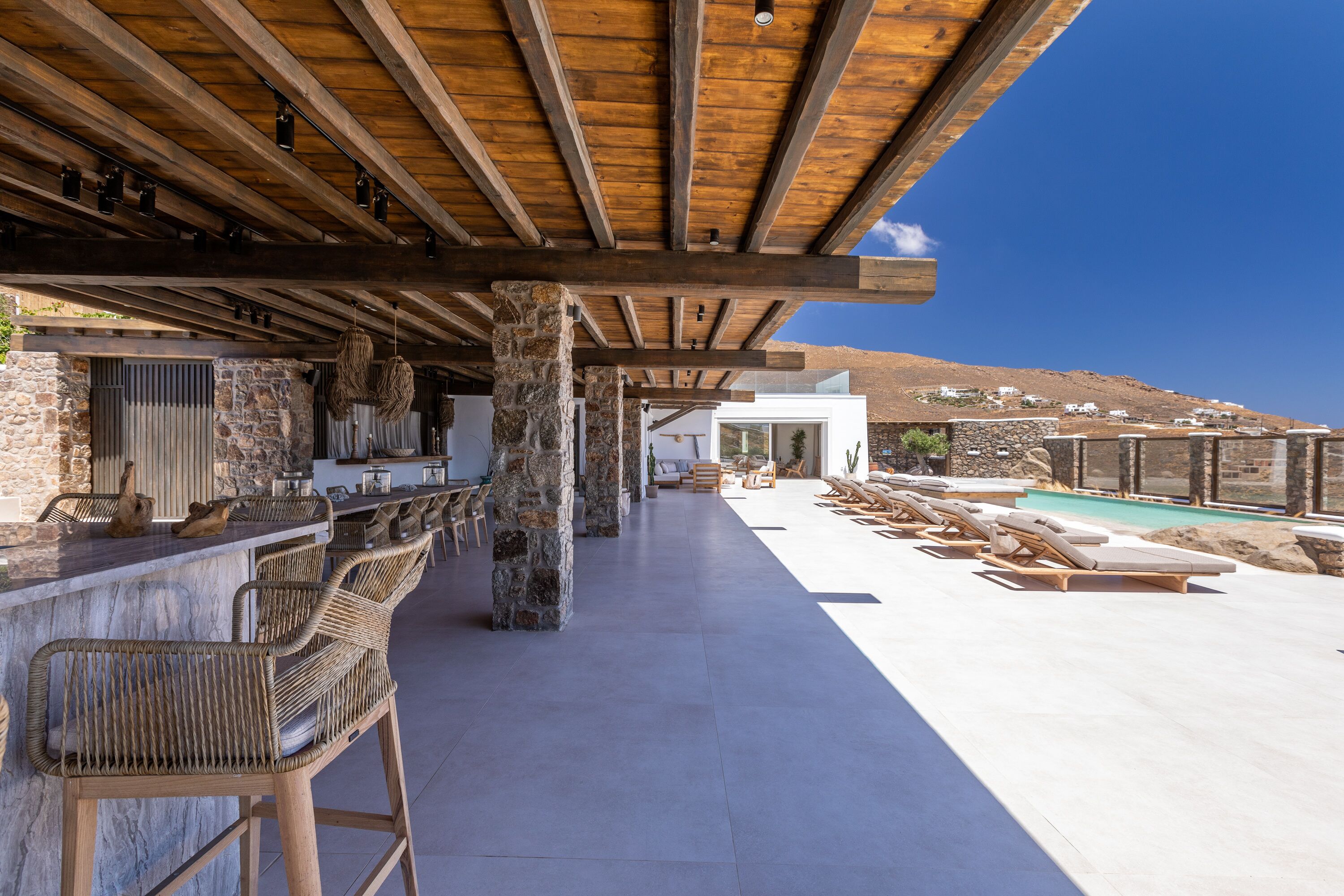 Un espacio al aire libre techado con un bar, asientos y una piscina.