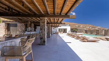 Un espacio al aire libre techado con un bar, asientos y una piscina.