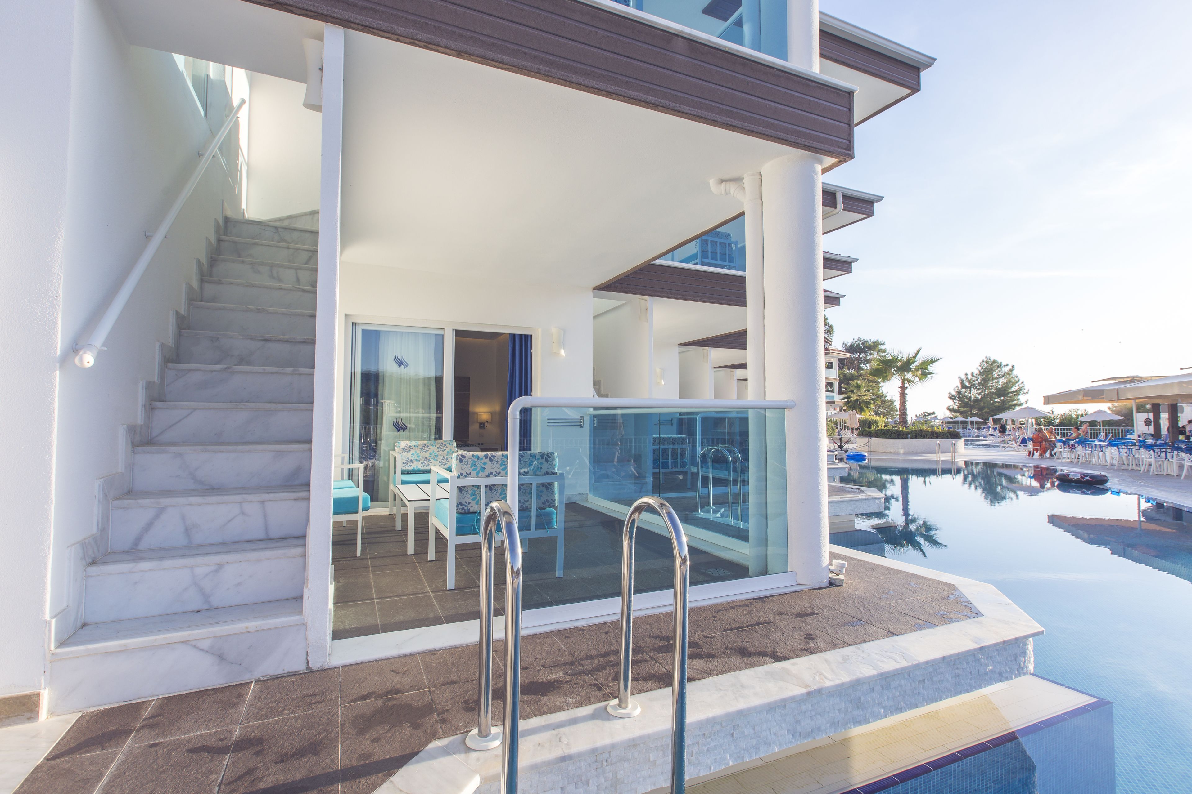 A modern hotel with a pool, a staircase, and a glass-enclosed lounge area.