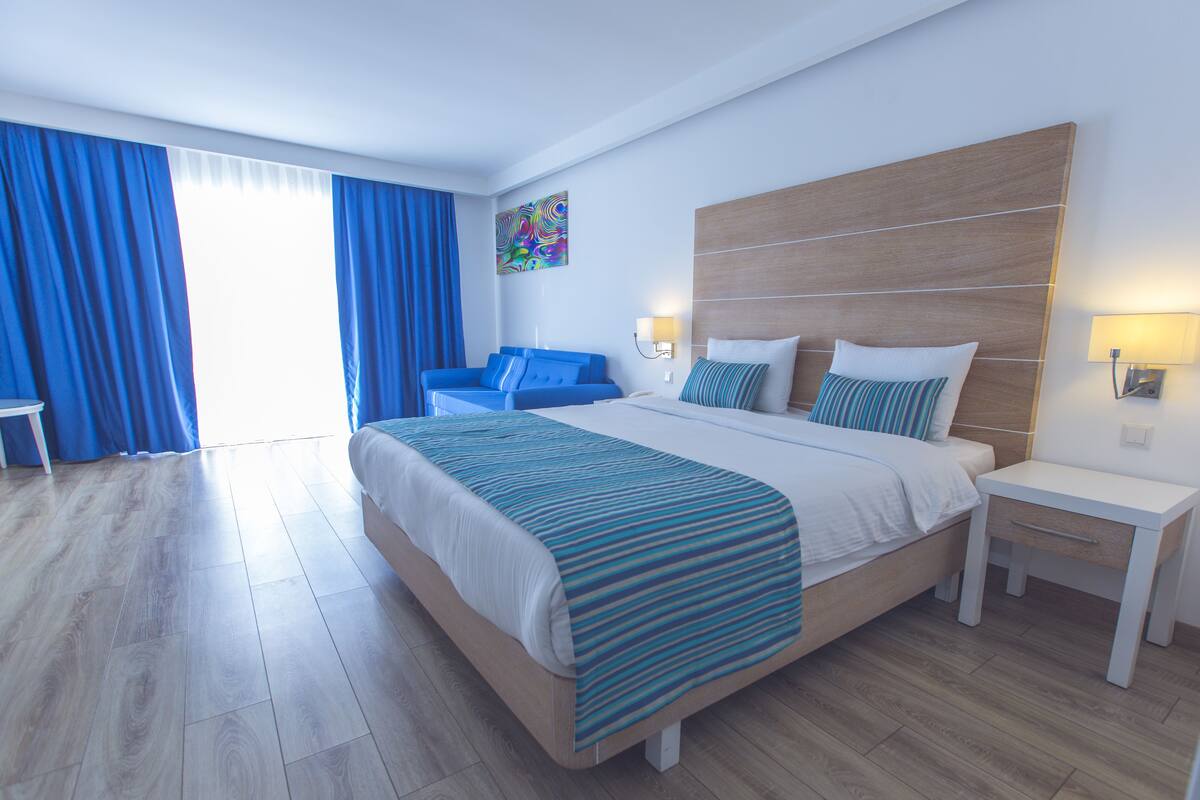 A modern hotel room with a large bed, a bedside table, a chair, and a view of the outdoors.