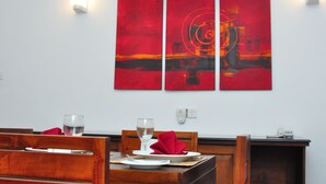 A dining area with a table set for two, featuring a red abstract painting on the wall, a white wall with a light switch, and a wooden chair. - Comfort@15 Hotel Colombo (Colombo)