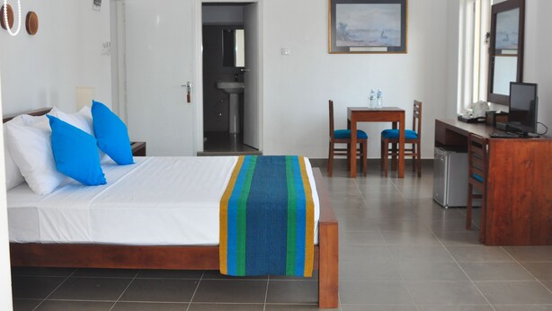 A hotel room with a bed, a desk, a chair, a small refrigerator, and a bathroom visible through an open door. - Comfort@15 Hotel Colombo (Colombo)