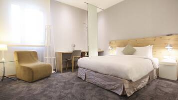 A hotel room with a large bed, a desk, a chair, and a standing lamp.