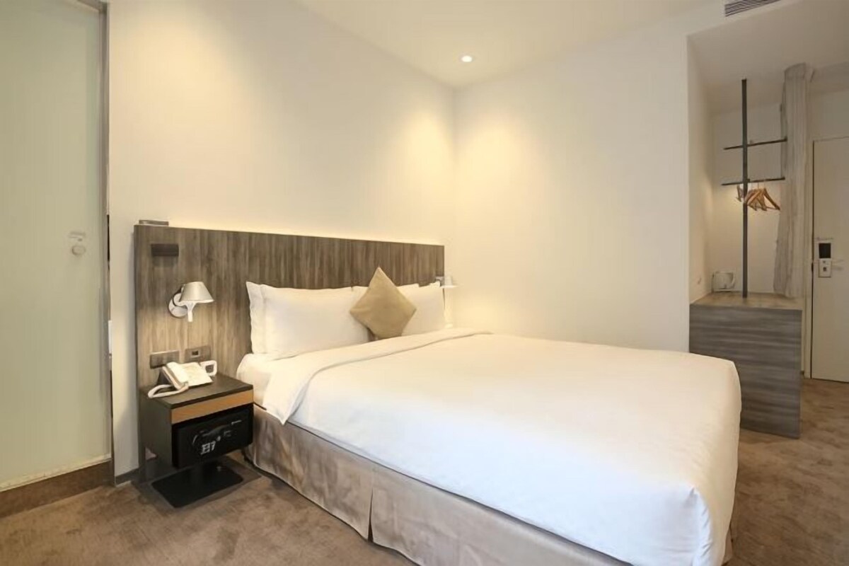 A hotel room with a large bed, a nightstand with a phone and lamp, and a staircase leading to another room.