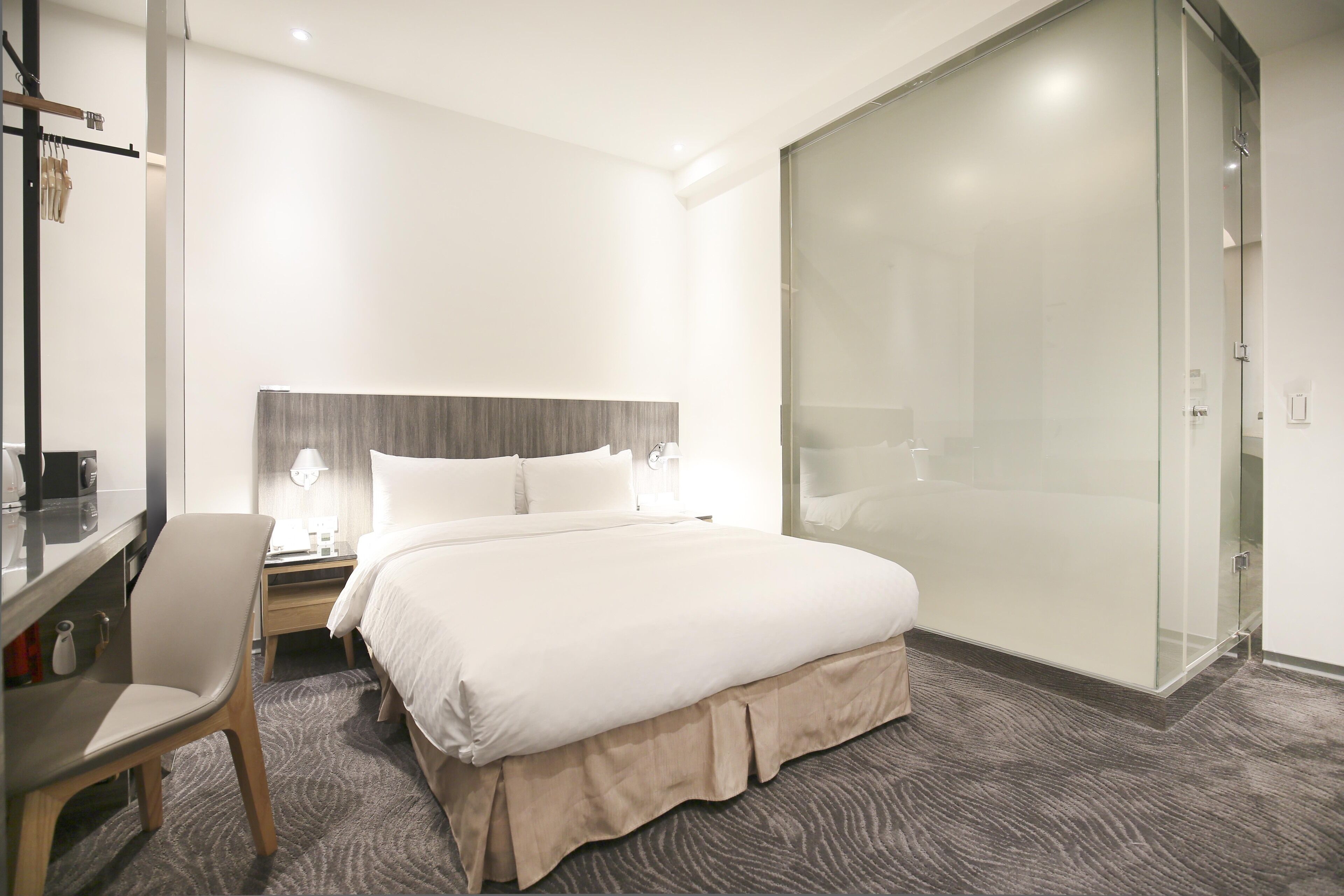 Une chambre d’hôtel comprenant un lit, un bureau, une chaise, une table de chevet et une cabine de douche en verre.