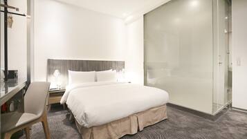 Une chambre d’hôtel comprenant un lit, un bureau, une chaise, une table de chevet et une cabine de douche en verre.
