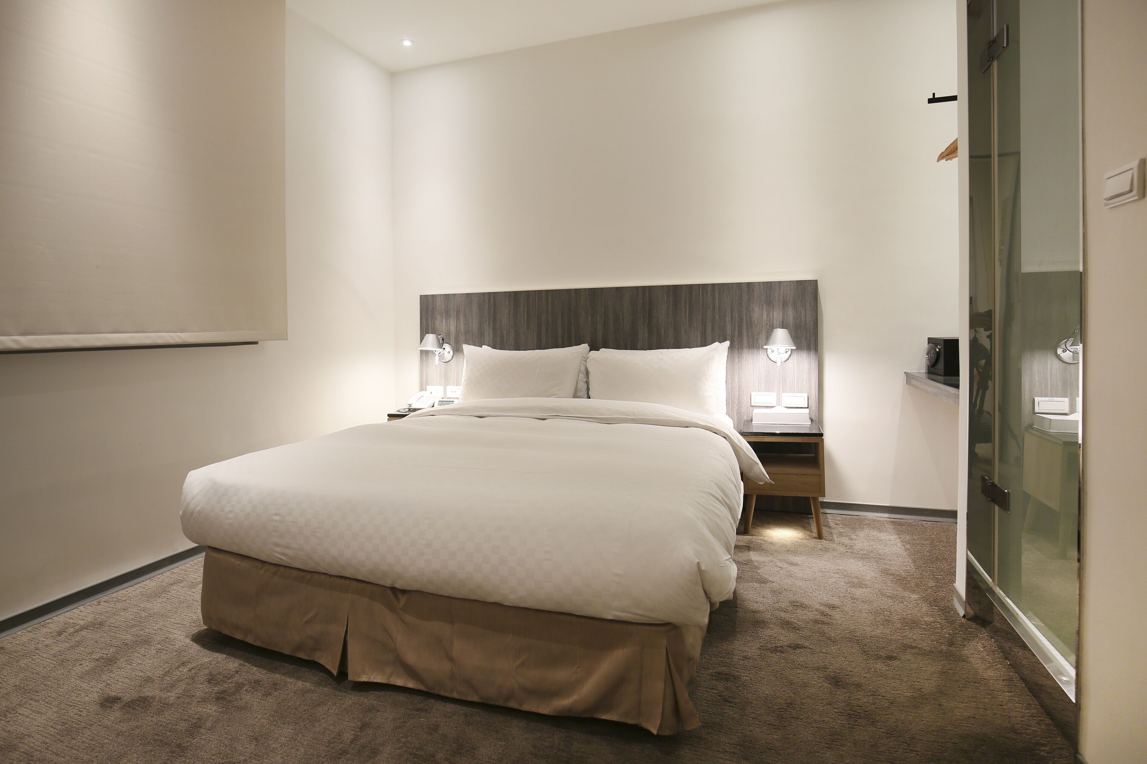 A hotel room with a large bed, bedside lamps, a nightstand, and a glass shower enclosure.