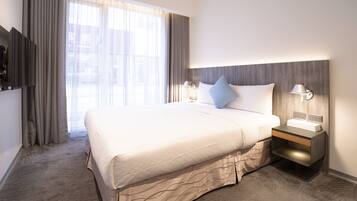 Et hotelværelse med en stor seng, et natbord med lampe og et fjernsyn ophængt på væggen.