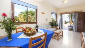 A dining area with a table set for two, a vase with flowers, and a view of palm trees through large windows. - Follow The Sun (Polis)