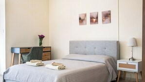 A bedroom with a bed, a nightstand, a lamp, and a dresser. - Follow The Sun (Polis)