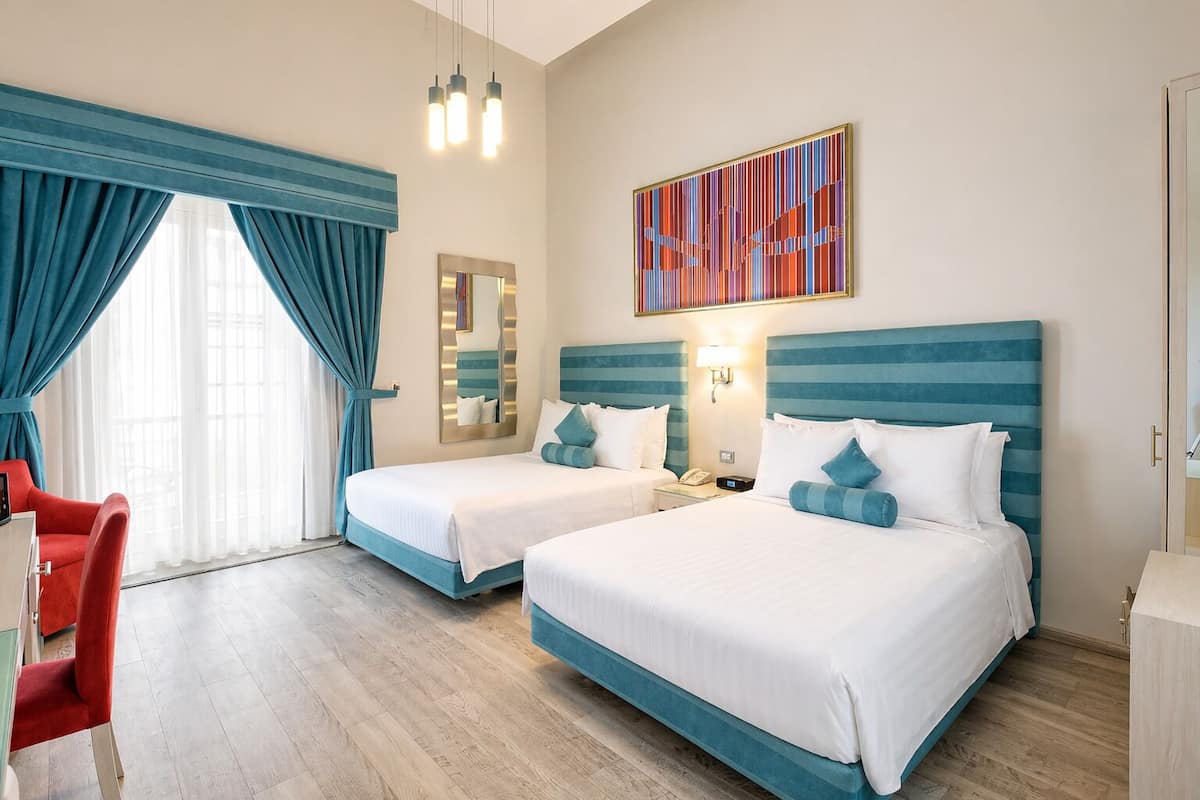 Una habitación de hotel con dos camas, una silla roja, un espejo y un cuadro en la pared.