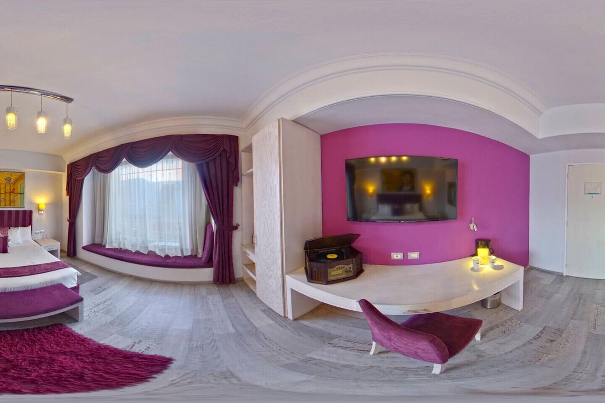 Una habitación de hotel moderna con distribución curva, una cama grande, un área de descanso con televisión y una pared de acento rosa brillante.