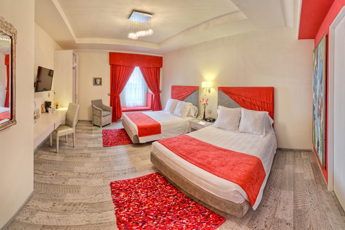 Habitación de hotel con dos camas, un escritorio, una silla, un televisor y una alfombra roja.