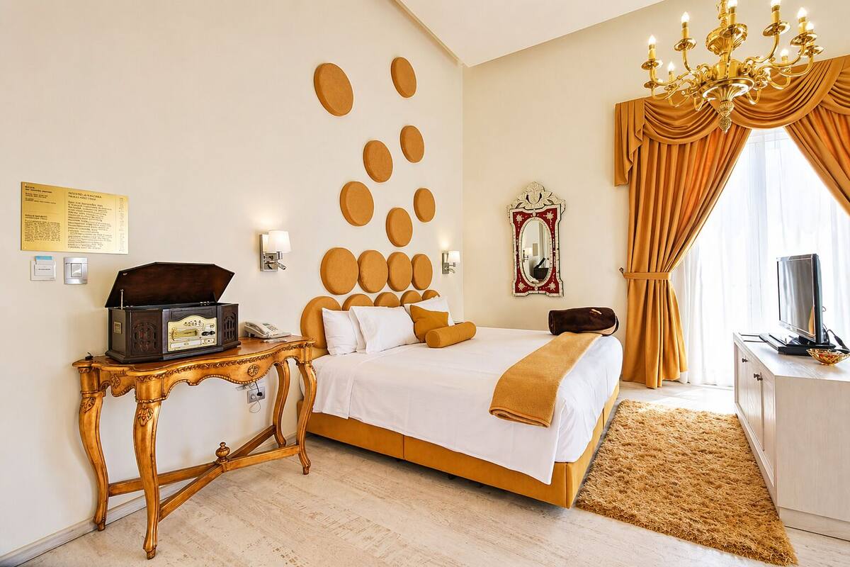 Habitación de hotel con cama, mesita de noche con radio, televisión, candelabro y un espejo grande.