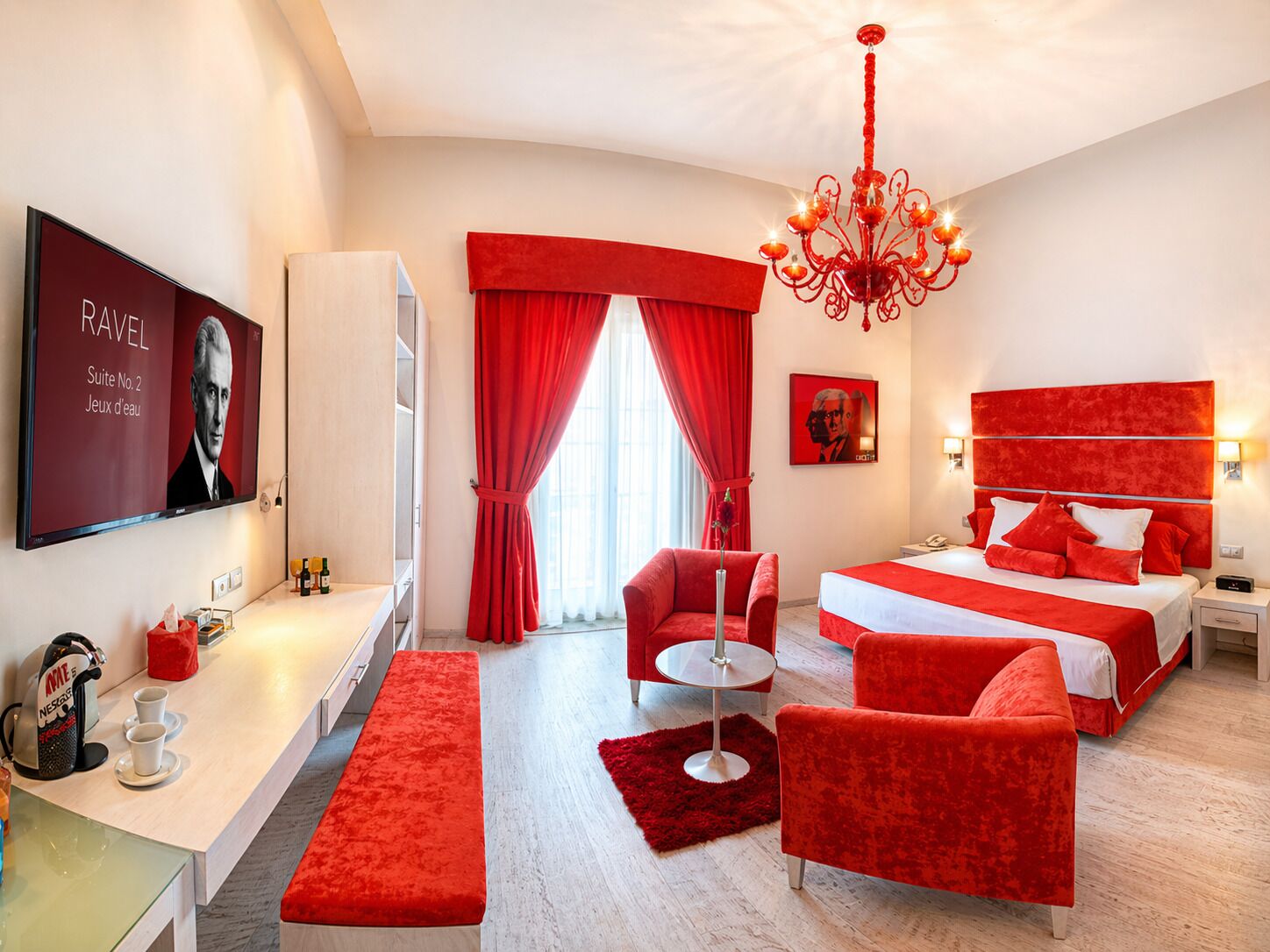 A hotel room with a bed, a desk, a chair, a red carpet, and a chandelier.