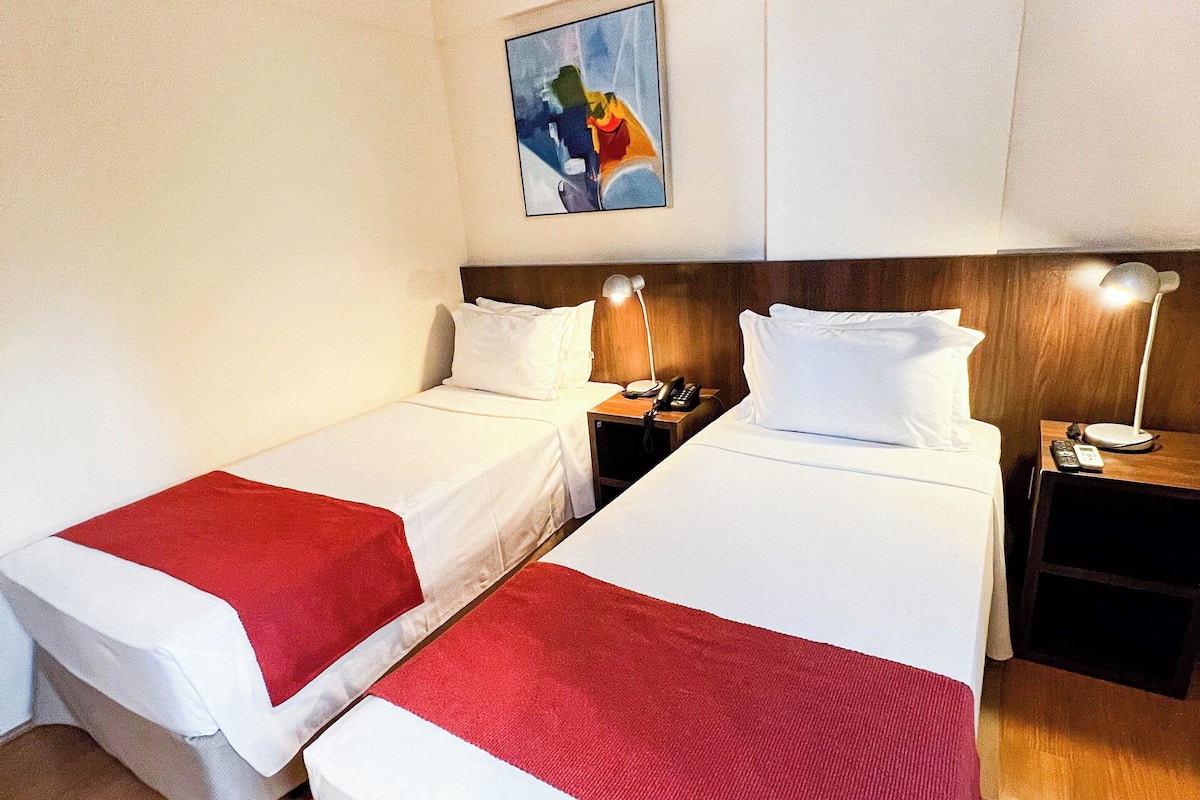 A hotel room with two beds, each with a red and white bedspread, wooden headboards, and bedside tables with lamps.