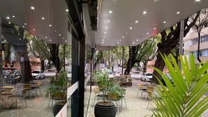 Terrassa exterior amb taules i caires, envoltada de plantes i arbres en testos.