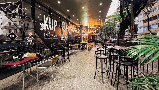Un cafè a l'aire lliure amb taules i caires, un cartell gran amb la inscripció "KUP café + bar", i un paviment de pedra.