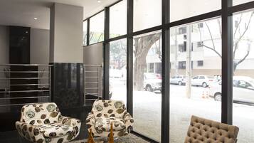 A modern lobby with large windows, a round glass table, two patterned armchairs, and a tufted sofa.