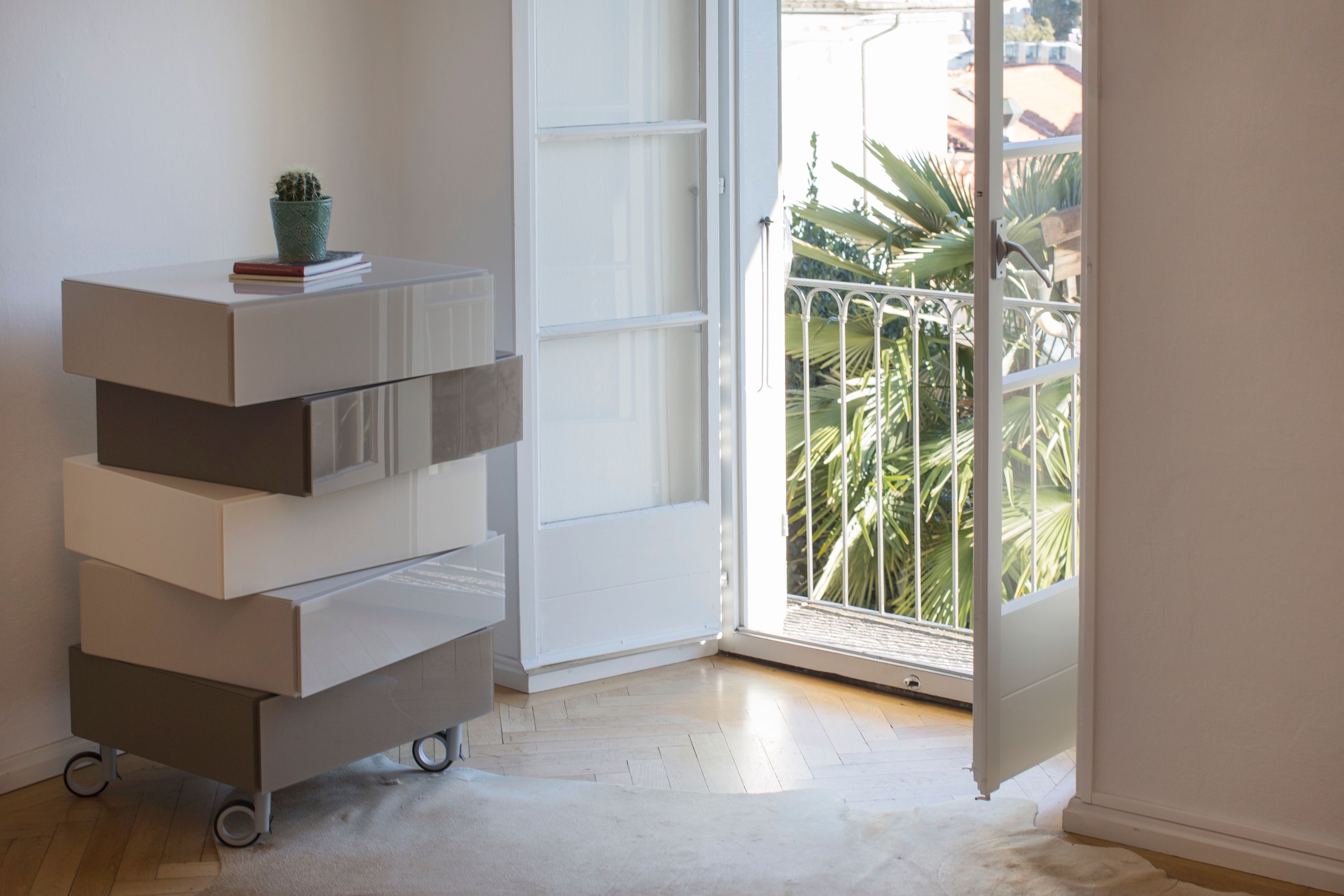 A minimalist room with a white storage unit, a sliding glass door leading to a balcony with plants.