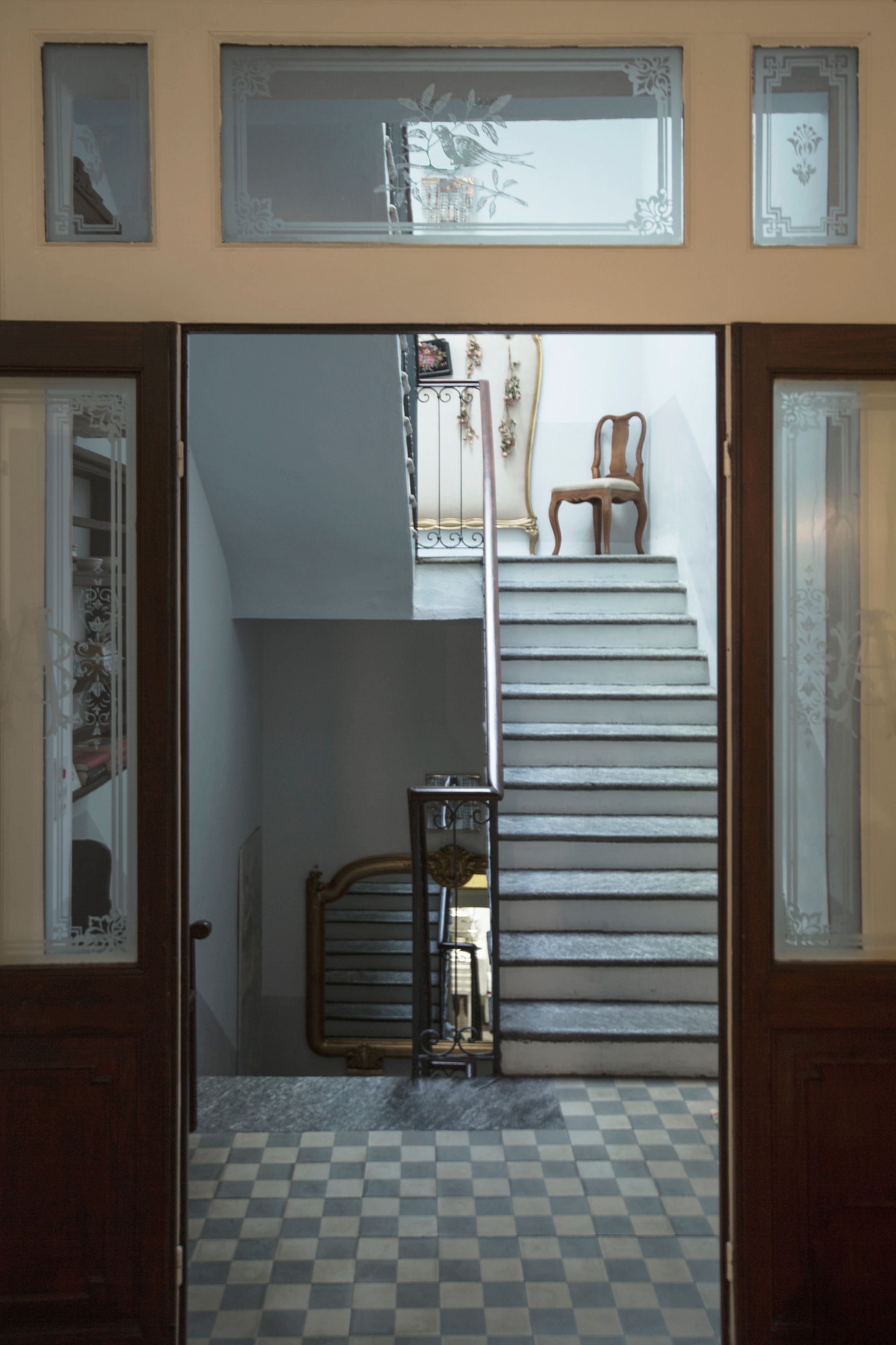 A staircase with a checkered floor, a metal railing, and a wooden chair at the top.