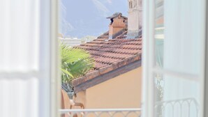 A view through a window of a building with a tiled roof, a brick chimney, and a mountain in the background. - Caffè dell'Arte Boutique Rooms Locarno (Locarno)