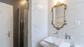 A modern bathroom with a glass-enclosed shower, a white sink, and a gold-framed mirror.