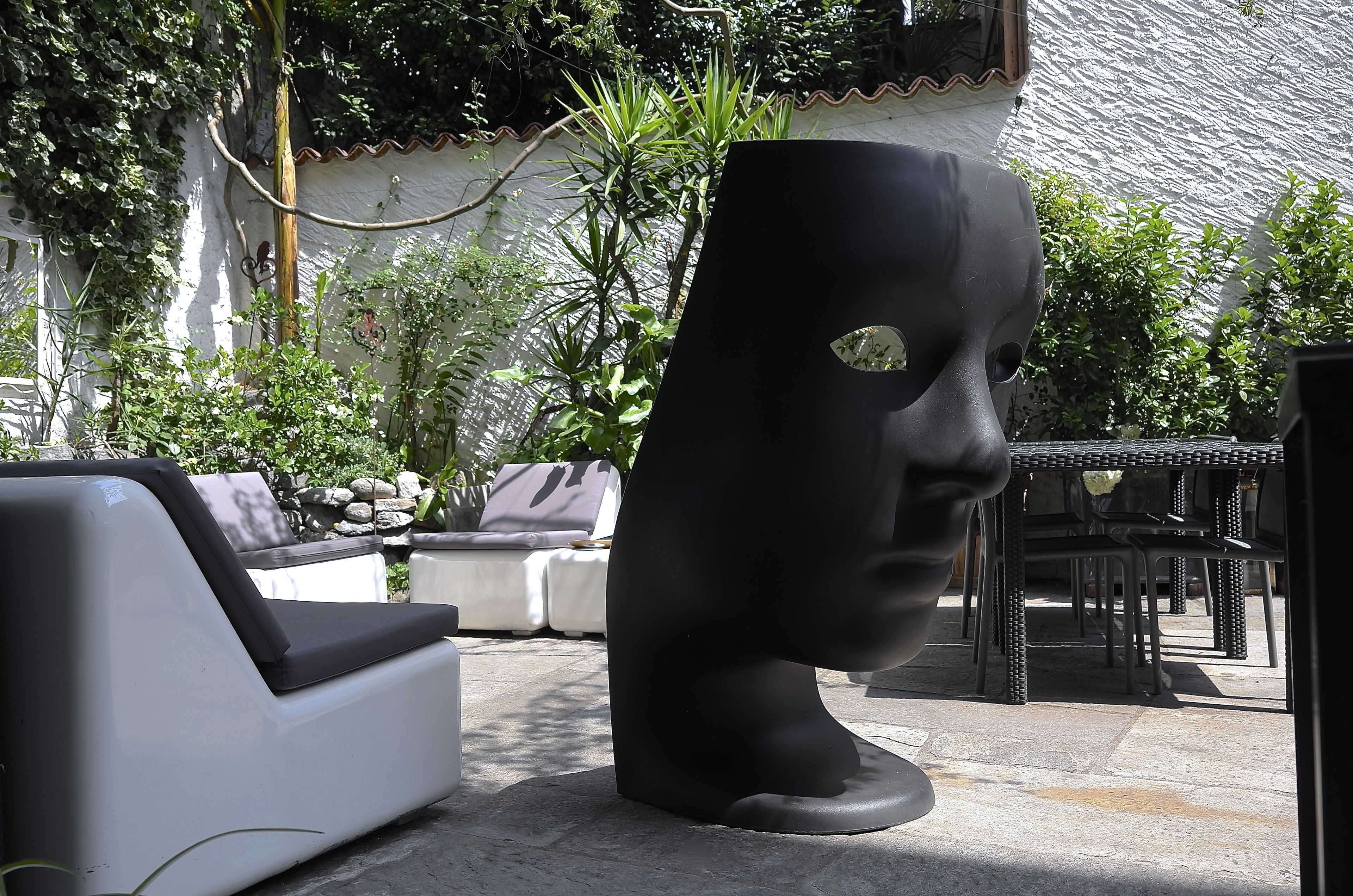 Un patio amueblado con mobiliario exterior, incluyendo un sofá blanco y una mesa de metal negro.