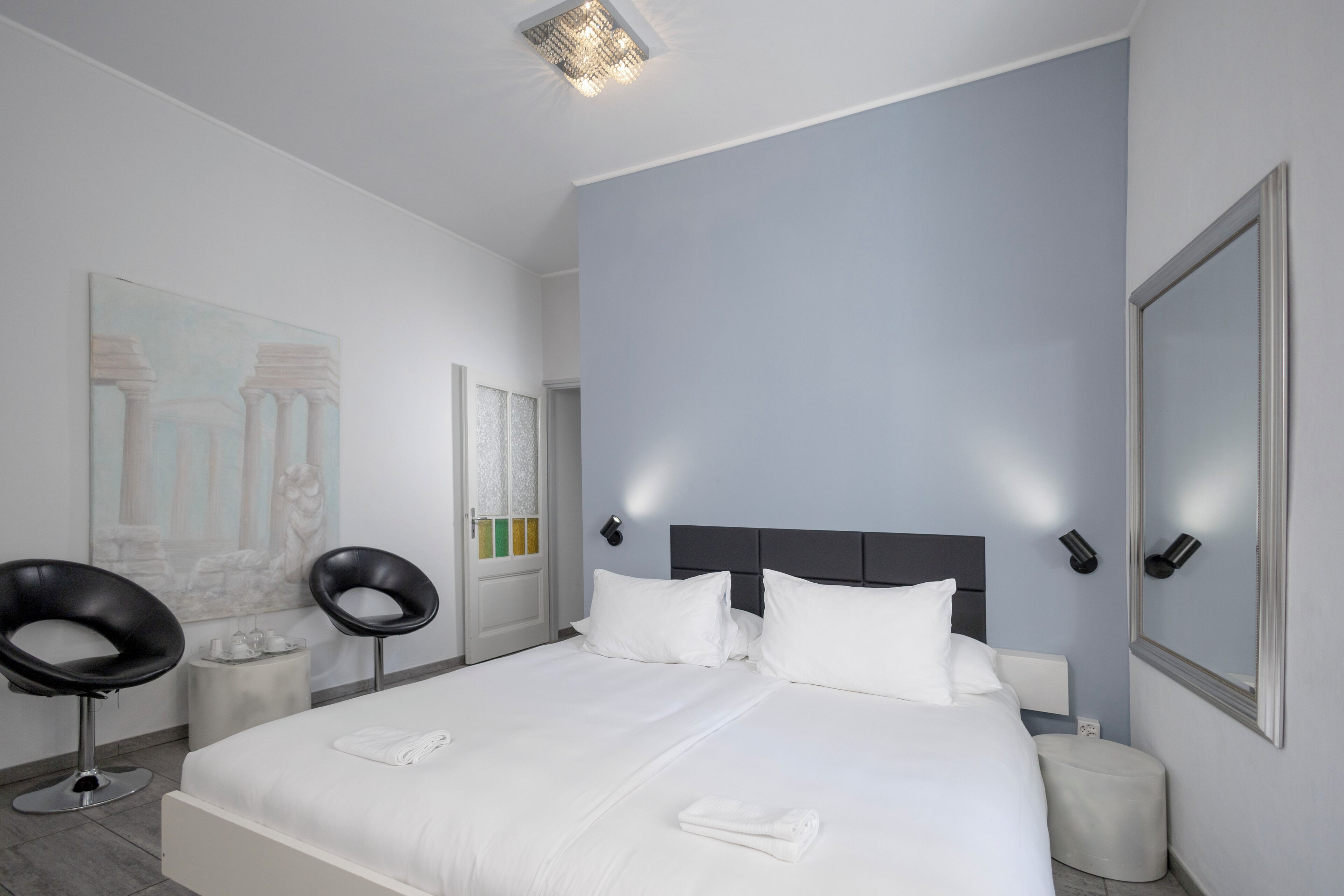 Ein modernes Hotelzimmer mit einem großen Bett, zwei schwarzen Stühlen, einem kleinen runden Tisch und einem großen Spiegel.