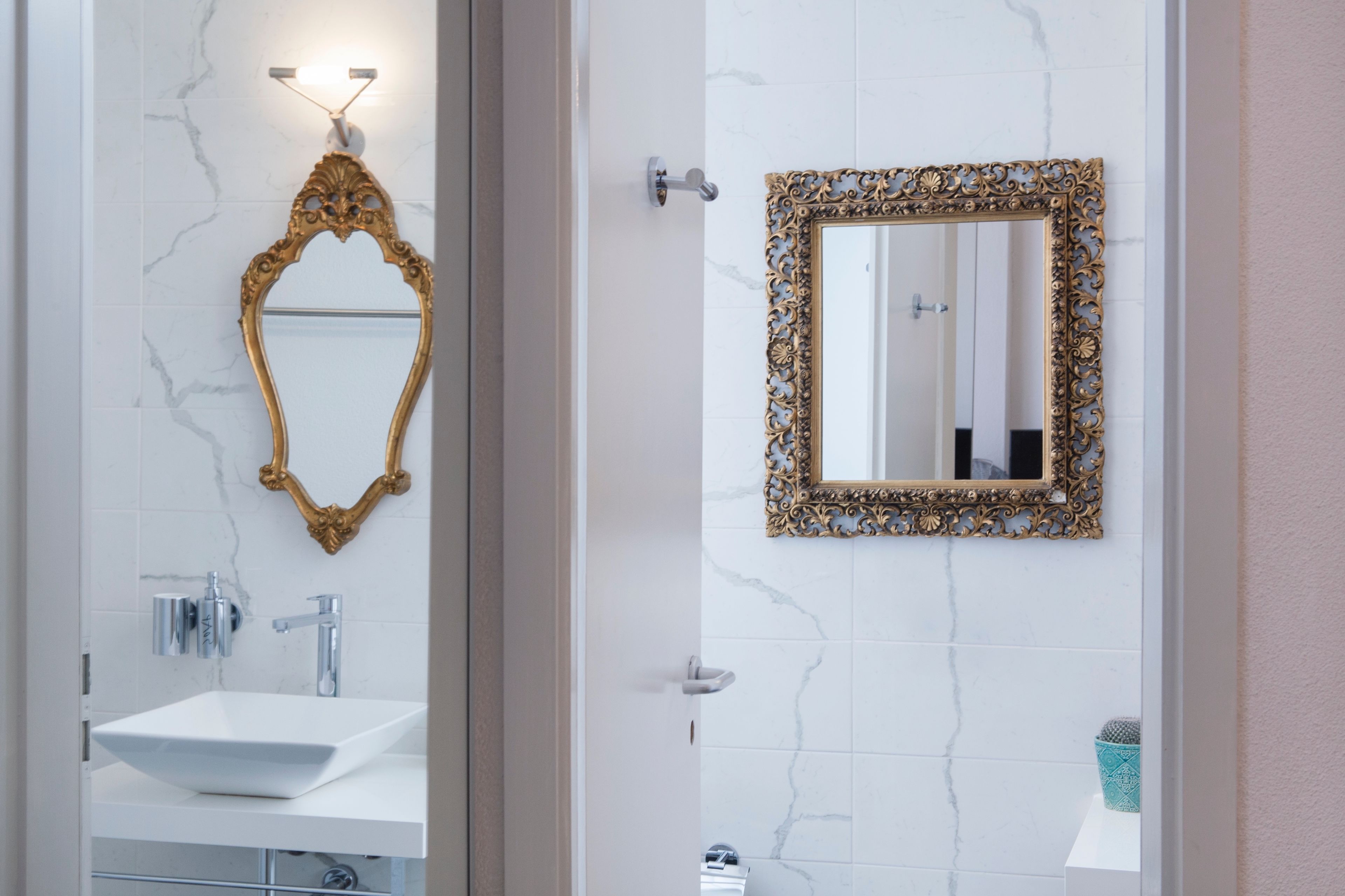 A bathroom with a white sink, a gold-framed mirror, and a white tiled wall.