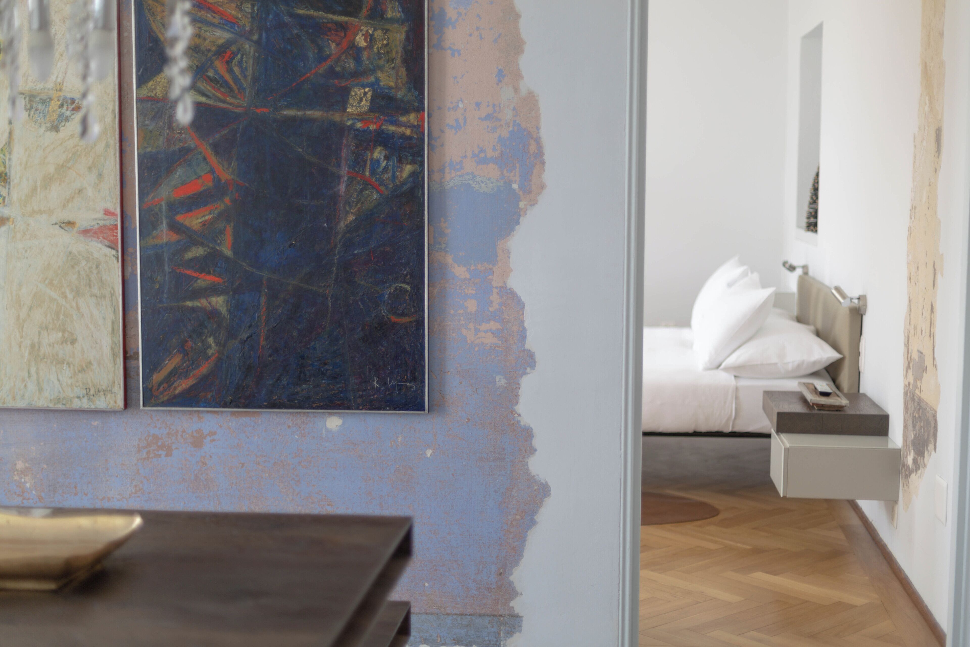 Une chambre à coucher moderne avec un lit, une table de chevet et un mur orné d’œuvres d’art abstraites.