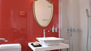 Un baño con un lavamanos blanco, un espejo con marco dorado y una pared con azulejos rojos.
