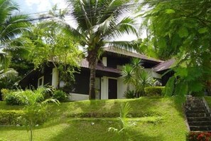 A house with a thatched roof surrounded by lush greenery and a well-maintained garden. - Pattaya Country Club (Bang Lamung)